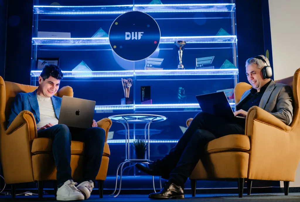 Doi colegi DWF lucrând pe laptop în zona lounge a biroului