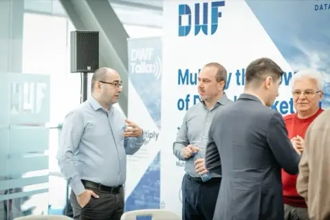 Participanți discutând în picioare, în fața bannerului DWF, înainte de atelier