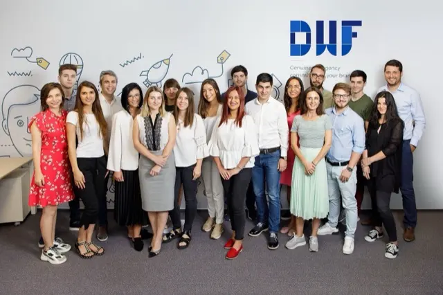 Fotografie de grup a echipei DWF, în fața peretelui cu logo-ul agenției