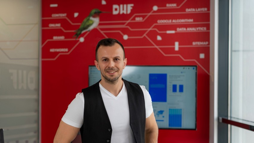 Fotografia publicată împreună cu anunțul noii divizii de Paid Media: un bărbat zâmbitor în biroul DWF, în fața unui perete roșu cu elemente de marketing digital