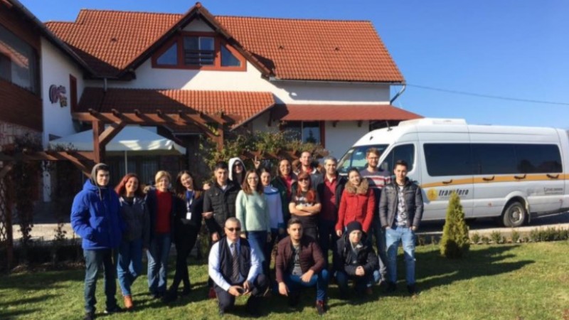 Echipa DWF, fotografiată în grup în fața unei pensiuni, lângă microbuzul cu care a călătorit la team building